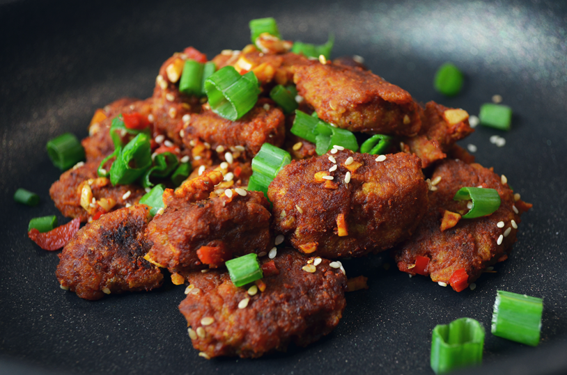 Vegan seitan pieces in chilli sauce topped with sesame seeds and spring onions